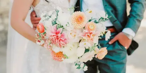 Bride holding a lush, custom wedding bouquet with pink and white flowers next to her groom.