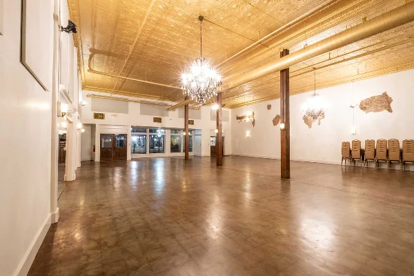 Interior view of the Robbins Sanford Grand Hall event space featuring a gold ceiling, chandeliers, and wooden columns.