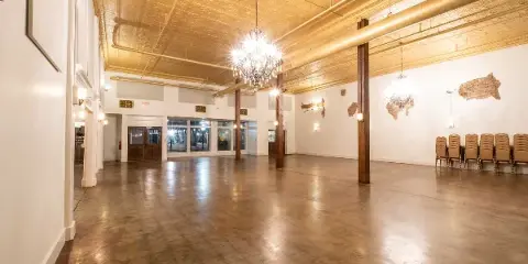 Interior view of the Robbins Sanford Grand Hall event space featuring a gold ceiling, chandeliers, and wooden columns.