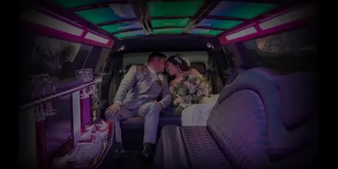 A bride and groom sitting together inside a luxury limousine with purple ambient lighting.