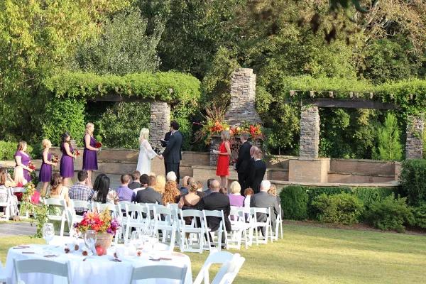 Outdoor wedding ceremony with bride and groom at an altar surrounded by guests and floral arrangements.