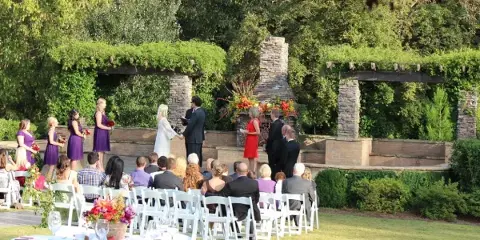 Outdoor wedding ceremony with bride and groom at an altar surrounded by guests and floral arrangements.