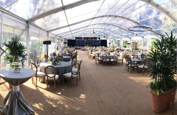 Interior of a clear event tent set up with round tables, chairs, and floral centerpieces.