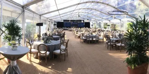 Interior of a clear event tent set up with round tables, chairs, and floral centerpieces.