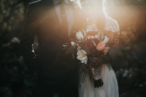 A cinematic wedding photograph of a couple holding a bouquet with warm backlighting.