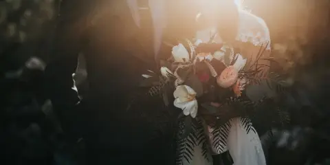 A cinematic wedding photograph of a couple holding a bouquet with warm backlighting.