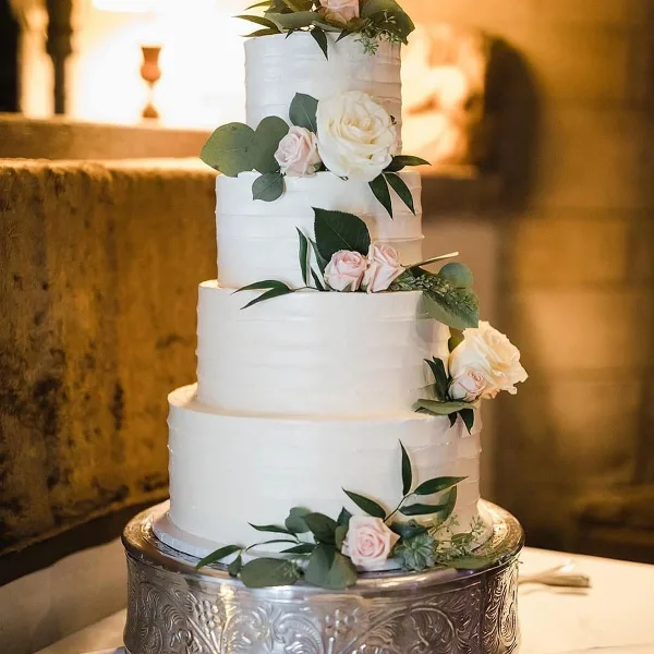 Four-tier white wedding cake with blush roses and trailing greenery