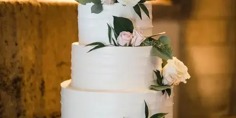 Four-tier white wedding cake with blush roses and trailing greenery