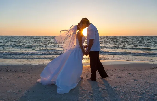 Bride and groom sharing a kiss on a beach at sunset
