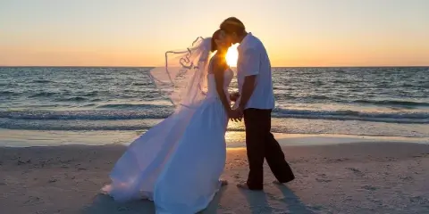 Bride and groom sharing a kiss on a beach at sunset