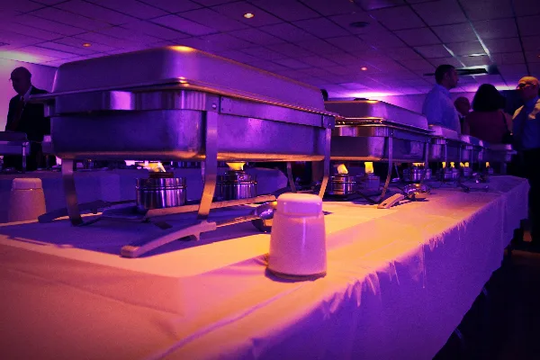 A catering buffet line featuring stainless steel chafing dishes on a table with a white tablecloth.