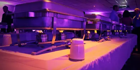 A catering buffet line featuring stainless steel chafing dishes on a table with a white tablecloth.