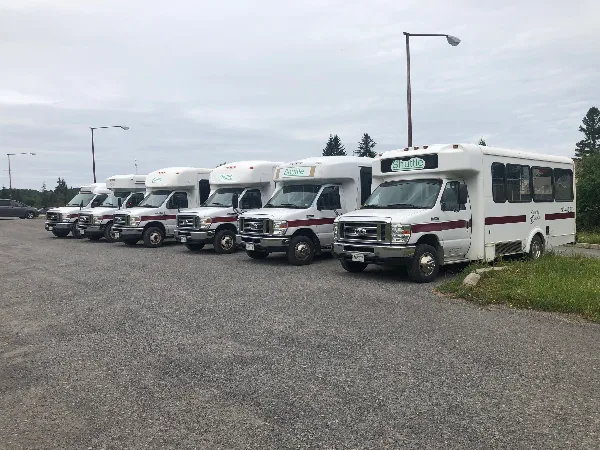 A row of white shuttle vans with maroon stripes and 'County Caravan' branding parked in a lot.