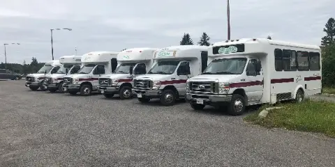 A row of white shuttle vans with maroon stripes and 'County Caravan' branding parked in a lot.