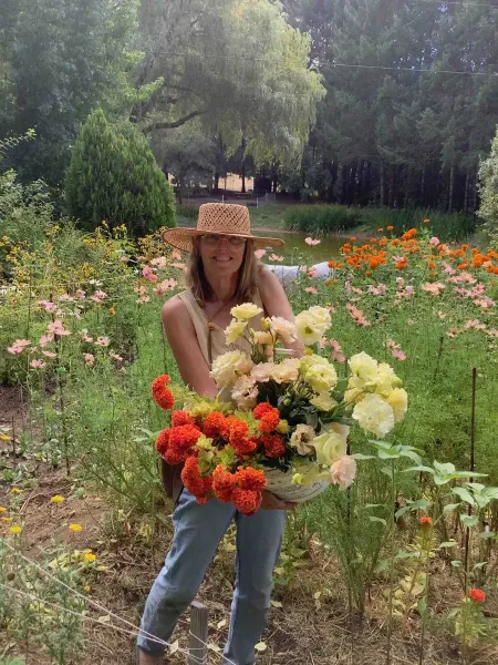 A woman in a straw hat holding a large bouquet of fresh flowers in a garden.