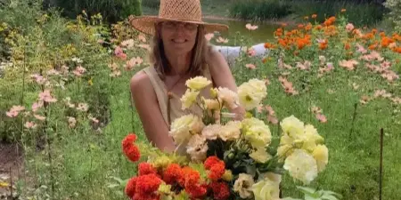A woman in a straw hat holding a large bouquet of fresh flowers in a garden.