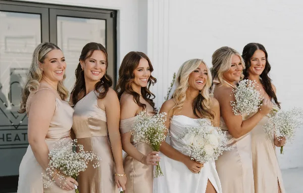 A bride and five bridesmaids with styled hair and makeup holding bouquets of white flowers.
