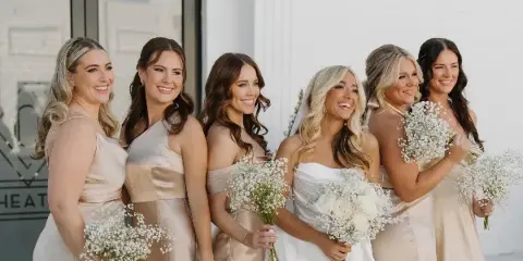 A bride and five bridesmaids with styled hair and makeup holding bouquets of white flowers.