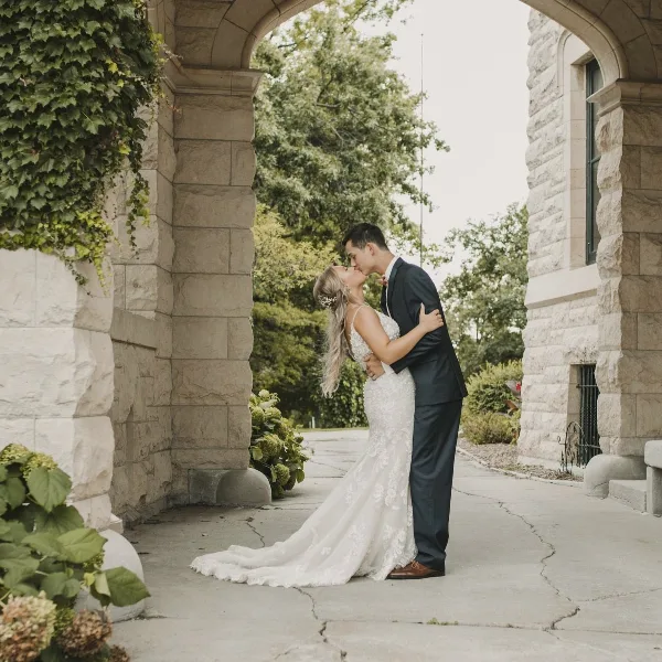 A bride and groom sharing a kiss under a stone archway with greenery.