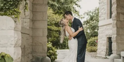 A bride and groom sharing a kiss under a stone archway with greenery.