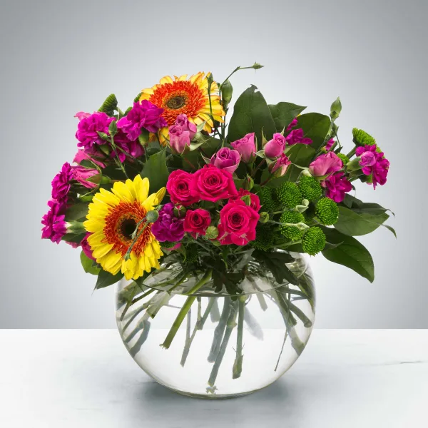 A vibrant mixed floral arrangement with pink roses, yellow gerberas, and purple carnations in a clear glass vase.