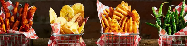 An assortment of prepared food items including sweet potato fries, potato chips, crinkle-cut fries, and green beans served in metal baskets lined with red and white checkered paper.