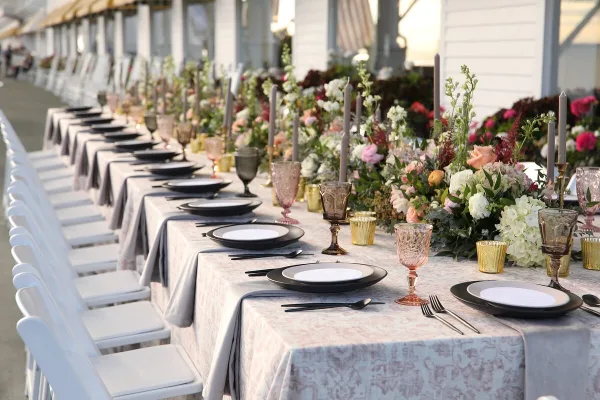 A long wedding reception table set with grey linens, black plates, and elaborate floral centerpieces.