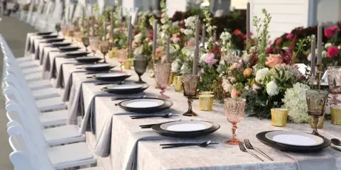 A long wedding reception table set with grey linens, black plates, and elaborate floral centerpieces.
