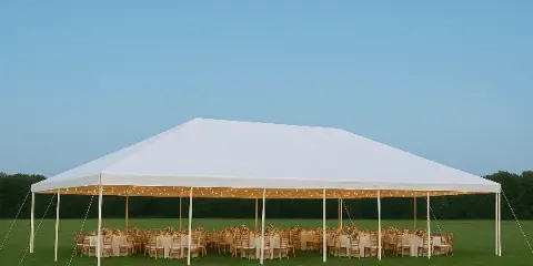 A large white event tent set up on a grassy field, containing rows of tables with white linens, wooden chairs, and string lights.