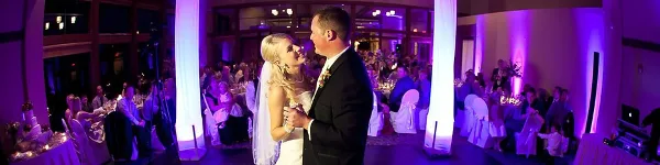 Wedding couple dancing at a reception with purple uplighting and a DJ setup in the background