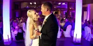 Wedding couple dancing at a reception with purple uplighting and a DJ setup in the background