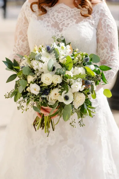 Bride in a white lace dress holding a lush white and green wedding bouquet
