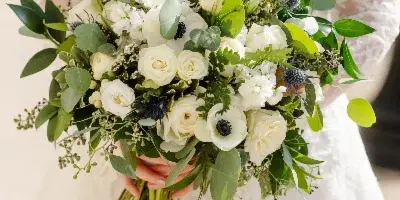 Bride in a white lace dress holding a lush white and green wedding bouquet