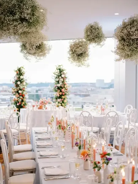 Elegant wedding reception table setting with hanging floral installations and white chairs.
