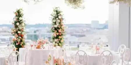 Elegant wedding reception table setting with hanging floral installations and white chairs.