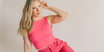 A woman with styled hair and makeup sitting on a studio floor wearing a pink top and pants.
