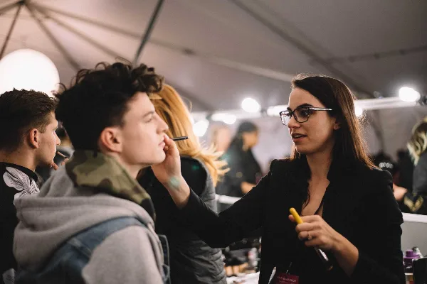 A makeup artist applying makeup to a client's face in a professional studio or event setting.