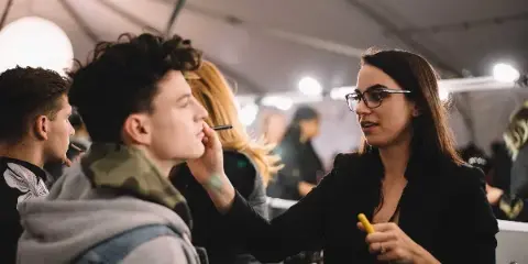 A makeup artist applying makeup to a client's face in a professional studio or event setting.