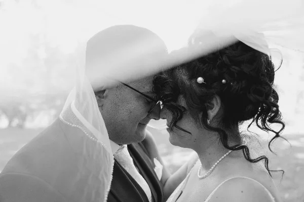 Black-and-white close-up of a bride and groom facing each other, with the bride's veil and pearl accessories visible.