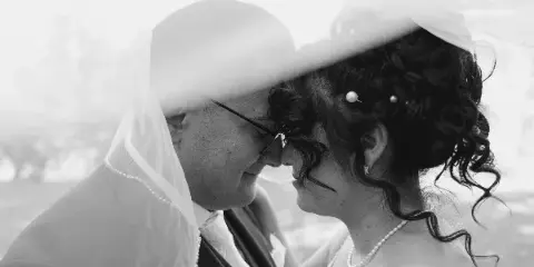 Black-and-white close-up of a bride and groom facing each other, with the bride's veil and pearl accessories visible.