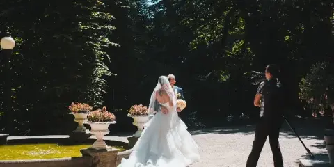 A videographer filming a bride and groom in a garden setting