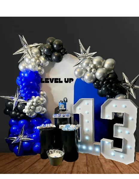 A blue, black, and silver balloon arch with star-shaped balloons and illuminated marquee numbers '13' on a wooden floor.