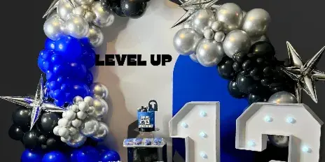A blue, black, and silver balloon arch with star-shaped balloons and illuminated marquee numbers '13' on a wooden floor.