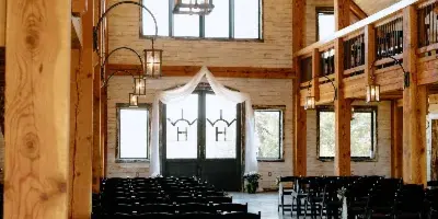 Interior view of a rustic timber-frame wedding barn with rows of black chairs and a chandelier.