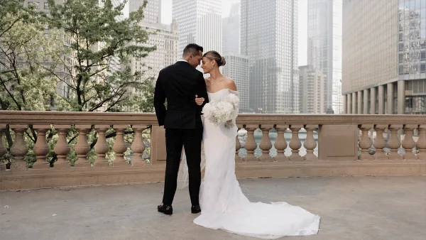 A bride and groom standing close together on a balcony with a city skyline in the background.