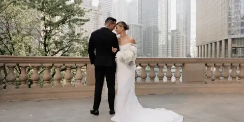 A bride and groom standing close together on a balcony with a city skyline in the background.