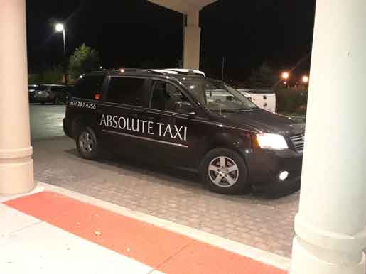 A black minivan with 'ABSOLUTE TAXI' branding parked at a curb at night.
