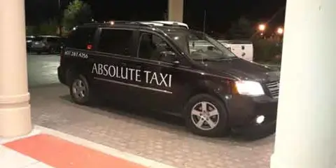 A black minivan with 'ABSOLUTE TAXI' branding parked at a curb at night.