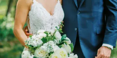 A bride with a styled updo and makeup standing next to a groom in a blue suit outdoors.
