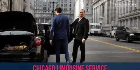 A professional chauffeur in a suit opens the door of a black sedan for a passenger on a city street.